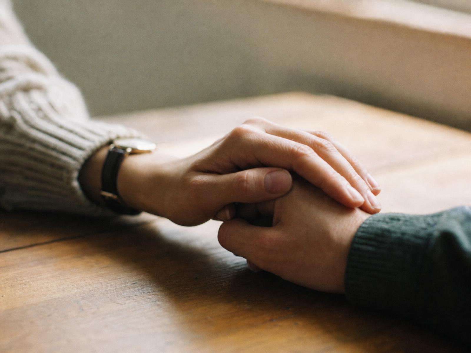 Two hands holding each other across a wooden table